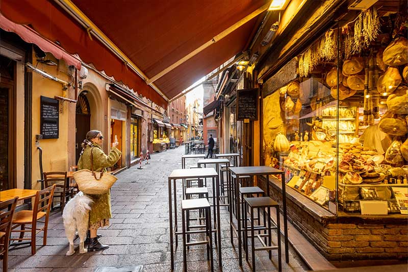 Reforma de tienda de barrio con encanto – Inteco Construcción Barcelona Tienda de barrio con escaparate reformado y zona exterior con mesas altas