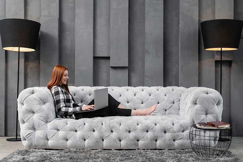 Mujer relajada trabajando desde el sofá en un salón moderno y funcional reformado por Inteco