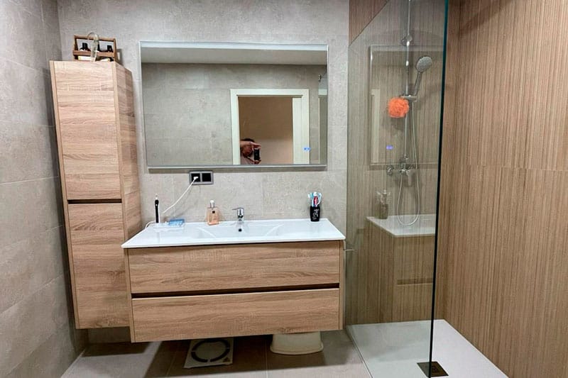 Baño moderno reformado con plato de ducha y muebles de madera en Chinchón.