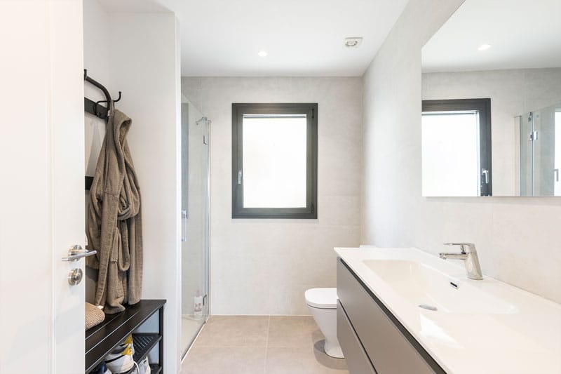 Baño secundario con ducha acristalada, mueble lavabo moderno y ventana con marco negro, obra de Inteco Construcción en Viladecavalls.