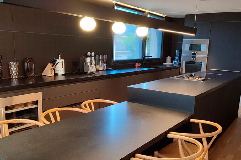 Cocina de diseño negro con isla central y sillas de madera en ático reformado en Passeig de la Bonanova, Barcelona.