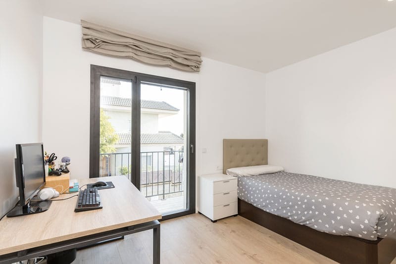 Dormitorio juvenil con escritorio, cama individual y acceso a balcón en vivienda unifamiliar construida por Inteco Construcción en Viladecavalls