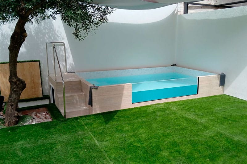 Piscina elevada en jardín con césped artificial como parte de la reforma integral de una vivienda en Chinchón por Inteco Construcción.