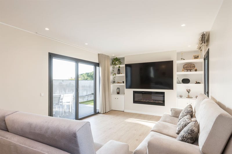 Salón principal con chimenea moderna, televisión de gran formato y salida al jardín en vivienda de obra nueva en Viladecavalls, construida por Inteco Construcción.
